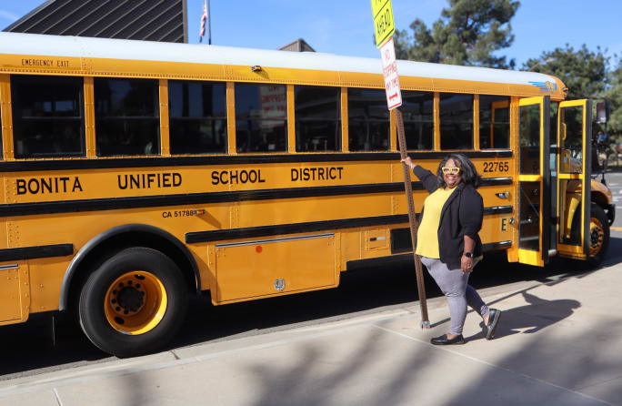 a woman stands in front of a school bus