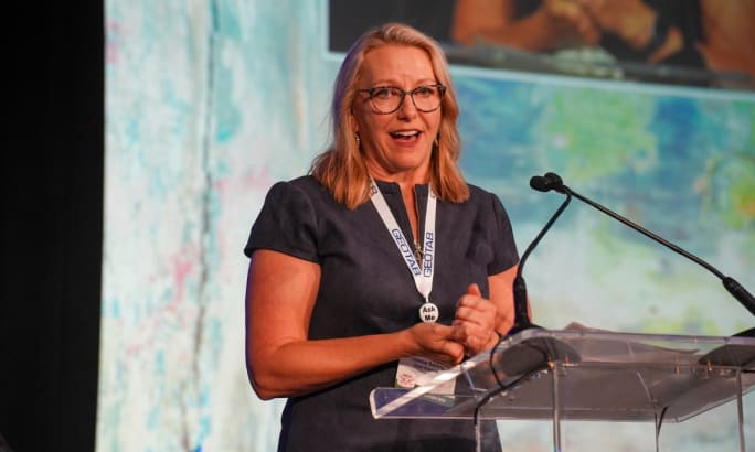 Theresa Belding on stage speaking at a podium.