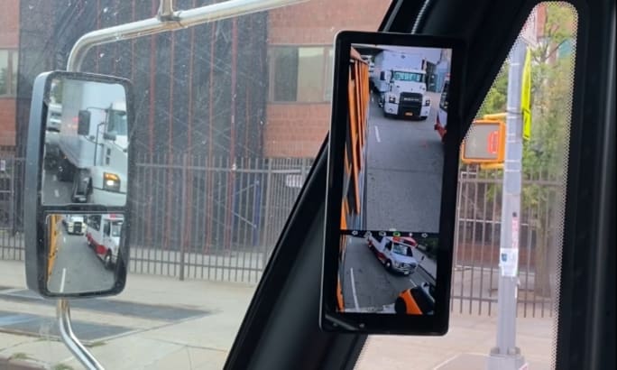 An e-mirror on the inside of a bus next to a normal mirror. 