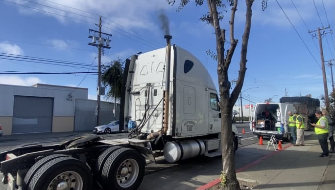 White semi truck with black smoke coming out of the exhaust at a CARB smoke check.