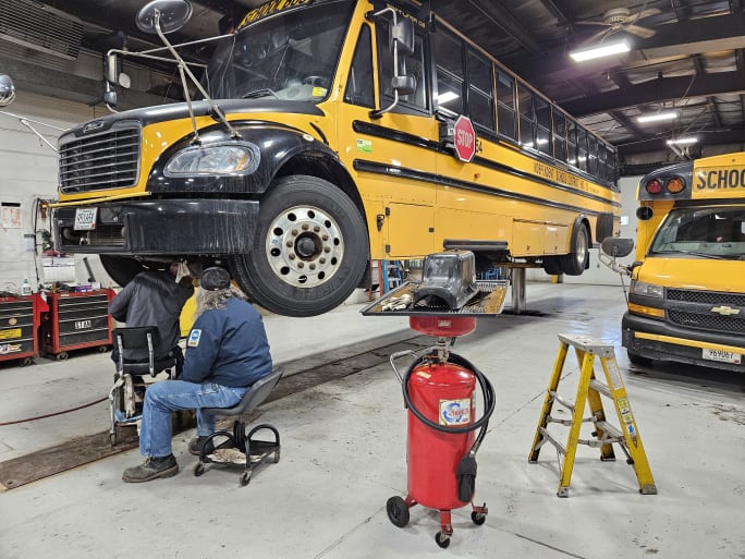 two people work under a school bus