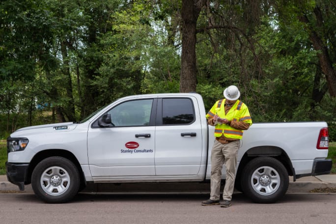 An employee stands in front of a white Ram 1500 pickup truck with the Stanley Consultants logo on the side.