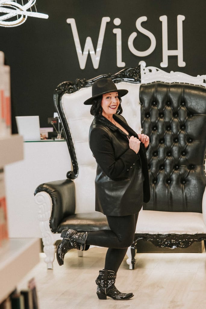 Hat on head and a booted foot up in the air, Rowena Yeager poses at Studio Wish Salon Spa.