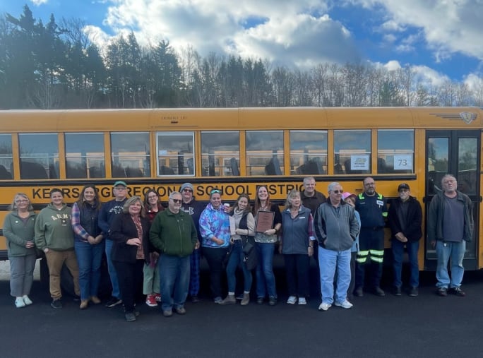a group of bus drivers stand in front of a school bus