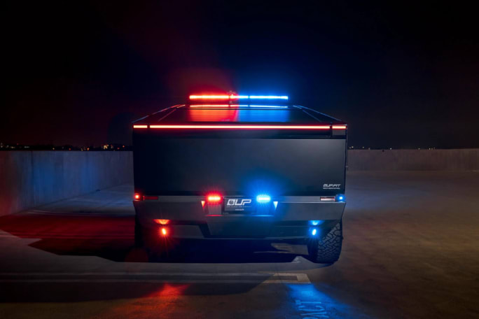 The rear of a Tesla Cybertruck is shown, upfitted with police equipment. Red and blue lights are engaged.