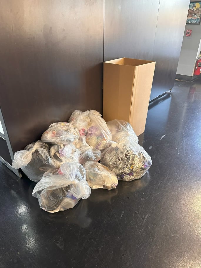 Bags of trash on the floor next to a cardboard collection box.