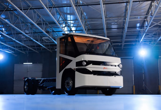 White electric chassis cab truck parked inside a warehouse with blue lighting in background