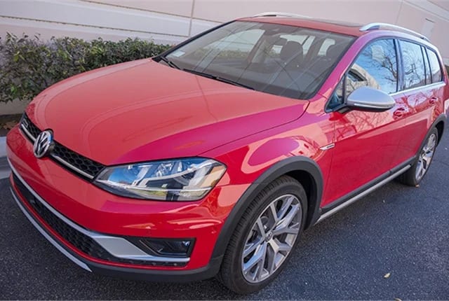 A red 2017 VW Golf Alltrack SEL sits on a road in front of a buliding.