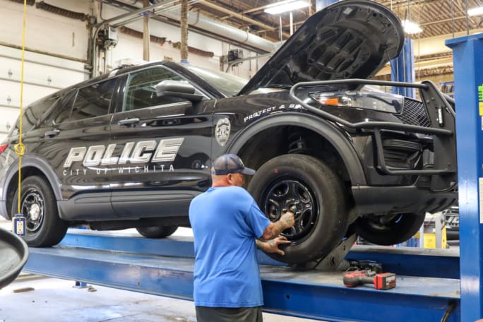 A technician works on the tire of a black Ford Police Interceptor Utility. 