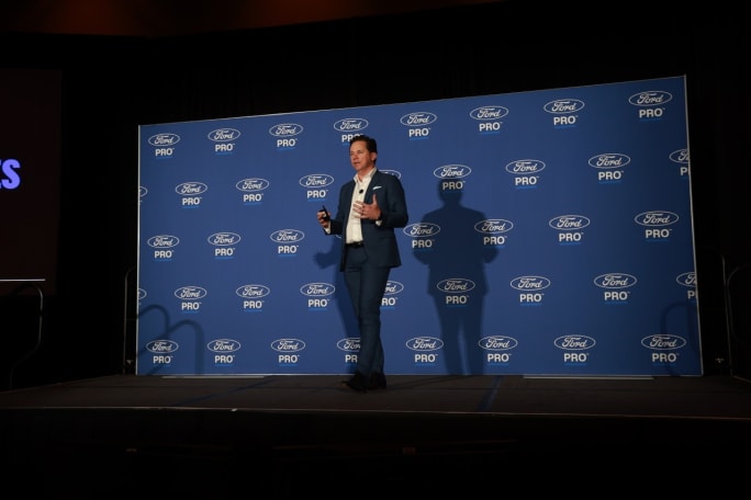 Matt Atkenson of Ford Pro presents on stage in front of a Ford Pro branded backdrop at Work Truck Week while discussing medium-duty truck fleet solutions.