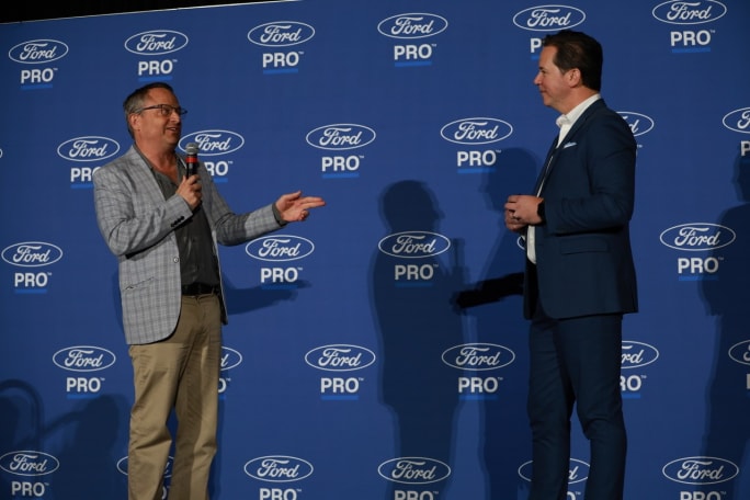 Chris Brown of Bobit/Fleet Group speaks into a microphone while standing on stage with Matt Atkenson of Ford Pro in front of a Ford Pro branded backdrop at Work Truck Week.