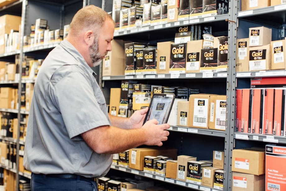 Man standing in front of parts shelf in workshop.