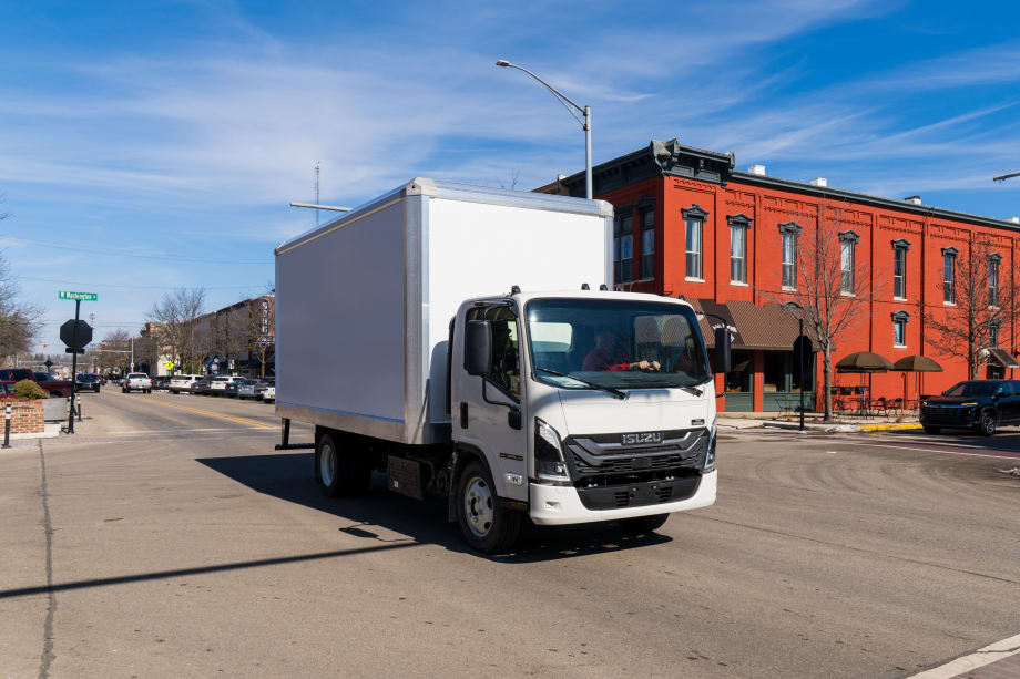 Isuzu commercial box truck driving in an urban area, representing a new body program with Aebi Schmidt that provides preconfigured, work-ready trucks for fleet customers.