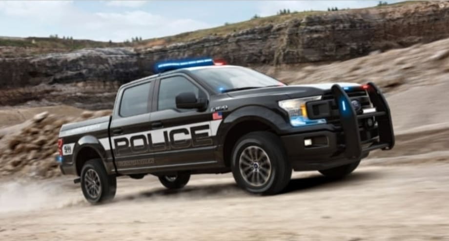 Black police pickup truck with emergency lights driving on rocky terrain
