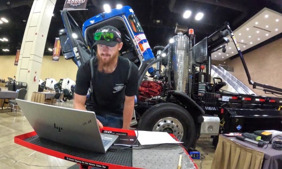 Male technician bent over a laptop computer in front of a line of CNG trucks in a maintenance shop.
