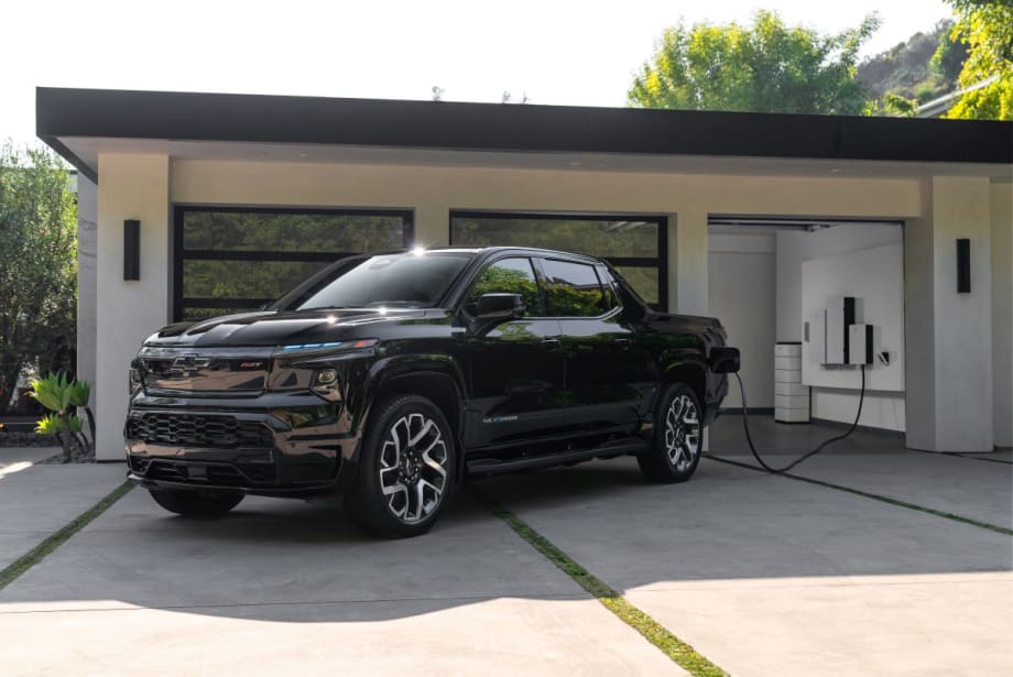Pickup truck sits outside luxury home's garage getting charged.