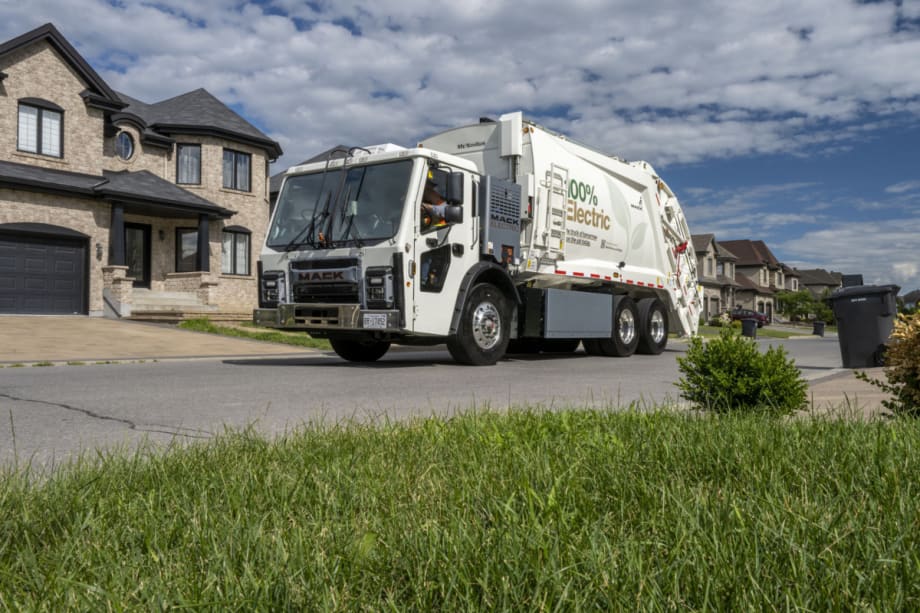 A white refuse truck, or garbage truck, drives down the road.