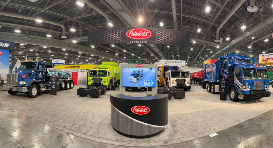 Four Peterbilt refuse trucks are parked in an exhibit space at WasteExpo.
