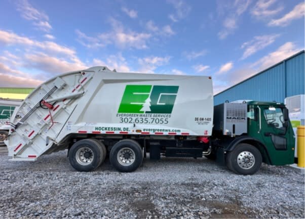 Electric refuse truck parked, facing right with EG logo on the side.