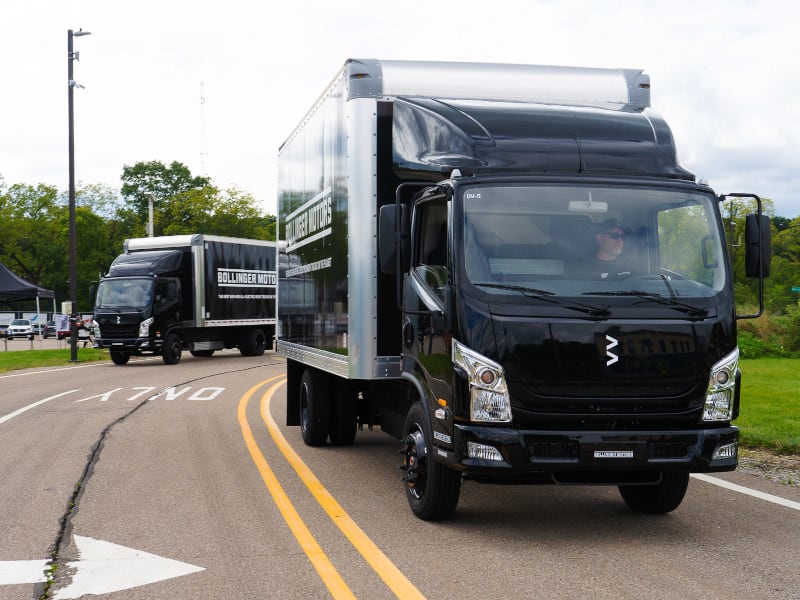 Two black-cab box trucks driving toward the camera.