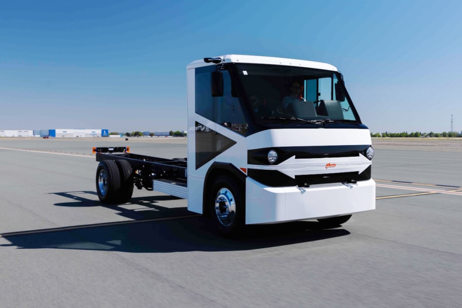 Front corner view of a white truck cap on a chassis parked at what looks like an airport.