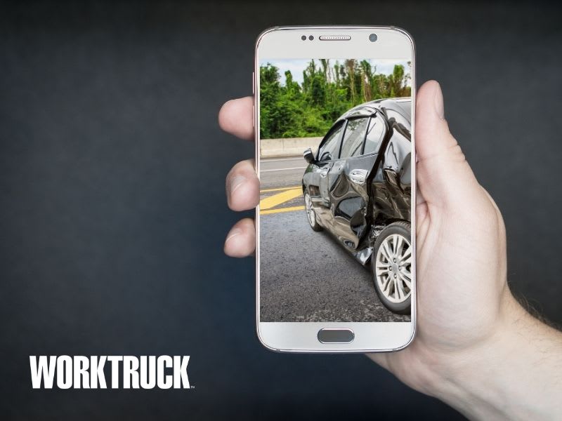 Person holding a cellphone with an image on the screen of a car that has been involved in a collision.
