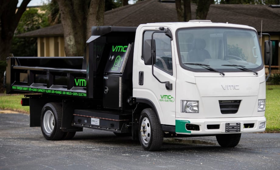 An electric truck with a white cab and a black bed is parked on a street.