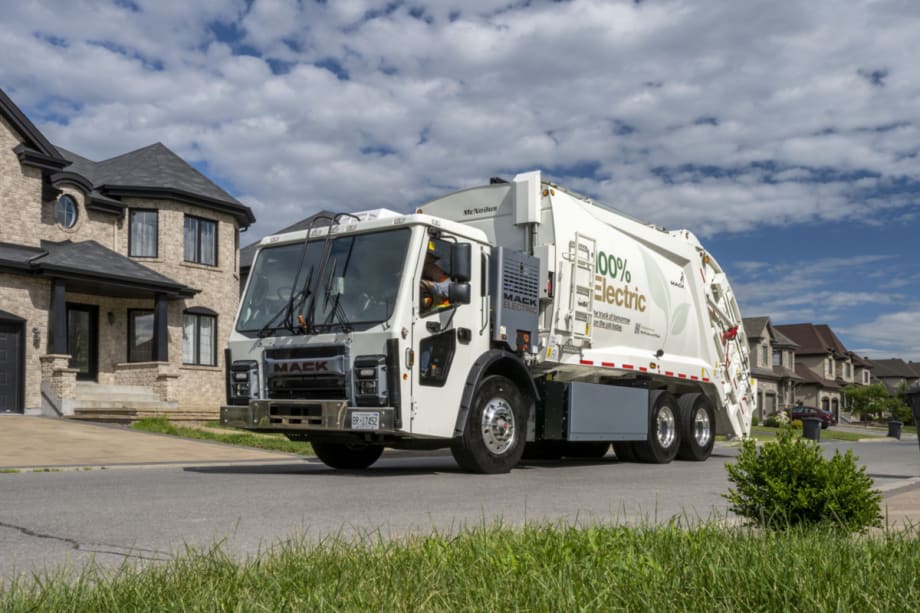 White refuse truck, garbage truck, drives down a residential street.