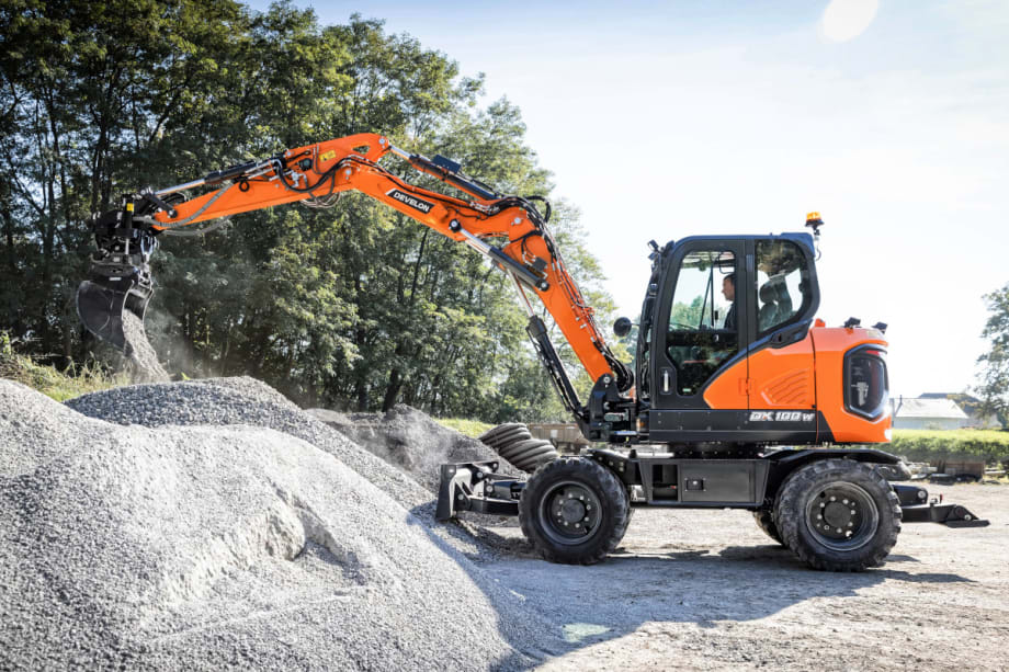 Orange wheel excavator is digging into a pile of gravel.