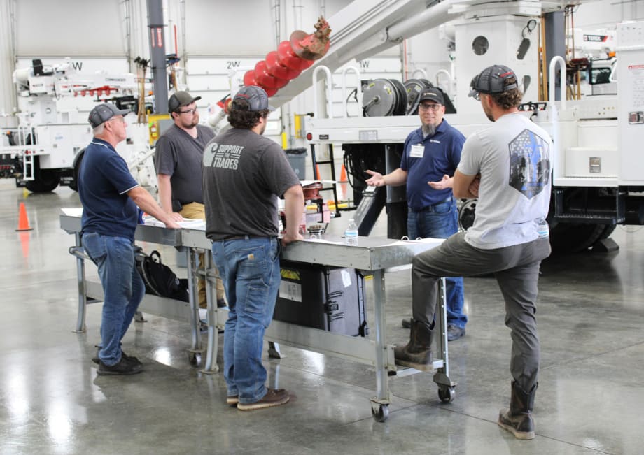 Men standing around a table in a warehouse, engaged in a discussion.