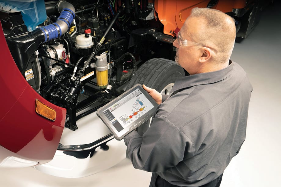 An man using a tablet to check the truck's engine.