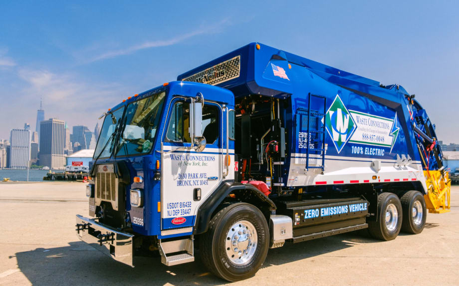 A blue and white garbage truck parked on the street.
