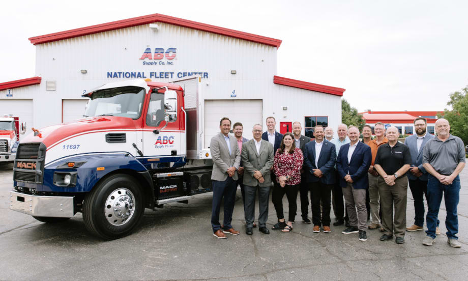 A group of people stands next to a medium-duty truck in front of a business, ABC Supply.