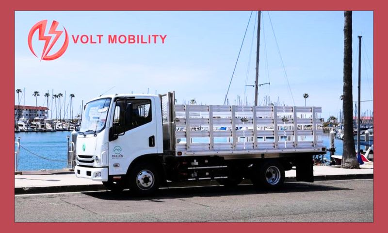 A Class 3 stake-body truck is parked in a parking lot in front of a marina, with the image also containing the logo for Volt Mobility.
