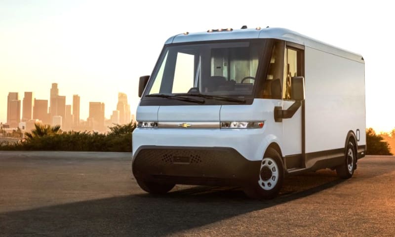 White EV delivery van in a parking lot with skyline behind it.