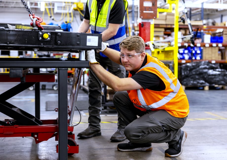 A man working diligently in a factory, surrounded by machinery and equipment, focused on his tasks.