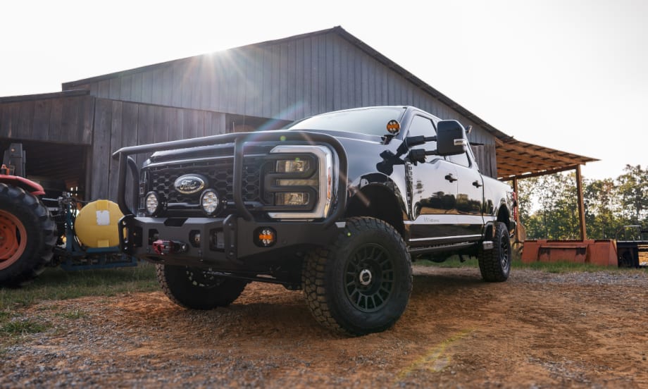 Angled view of a lifted black pickup truck parked in front of a barn.