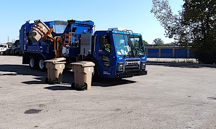Refuse truck with side loader lifting a garbage can.