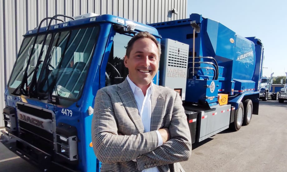 business attired man standing in front of a blue refuse truck
