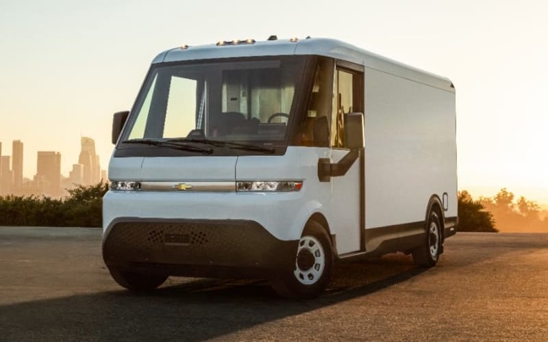 White electric delivery van parked in front of a city skyline.