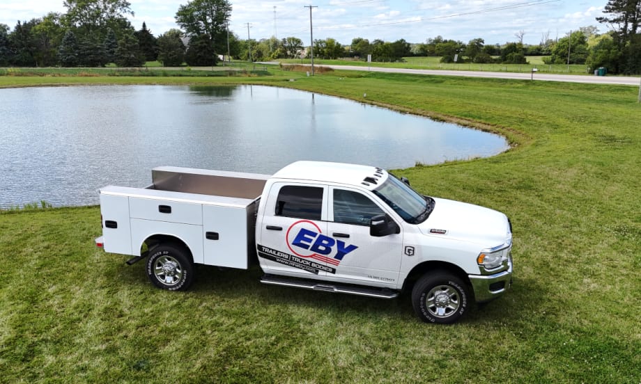 White truck with service body parked by a lake with Eby logo on side in blue.