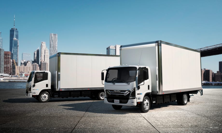 Two white box trucks parked in front of a city skyline.