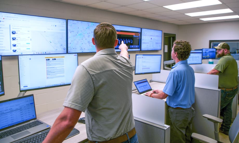 Group of men standing and monitoring computer screens.