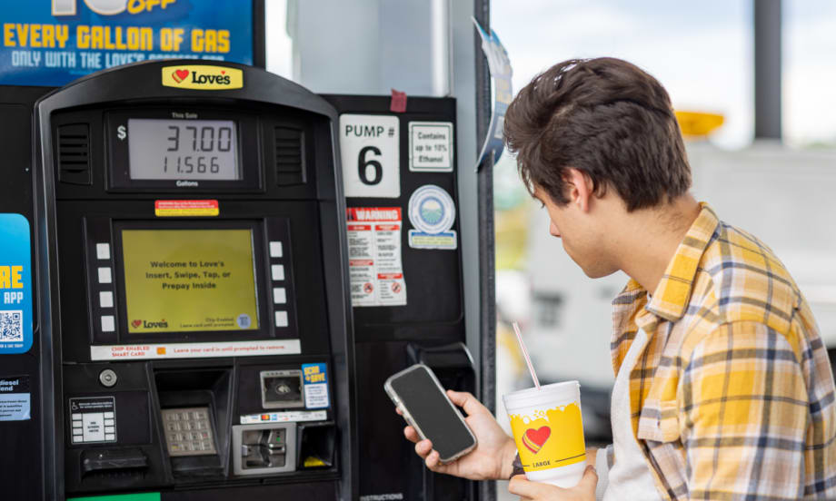 Young man looks at a fuel discount app while at a fuel pump.