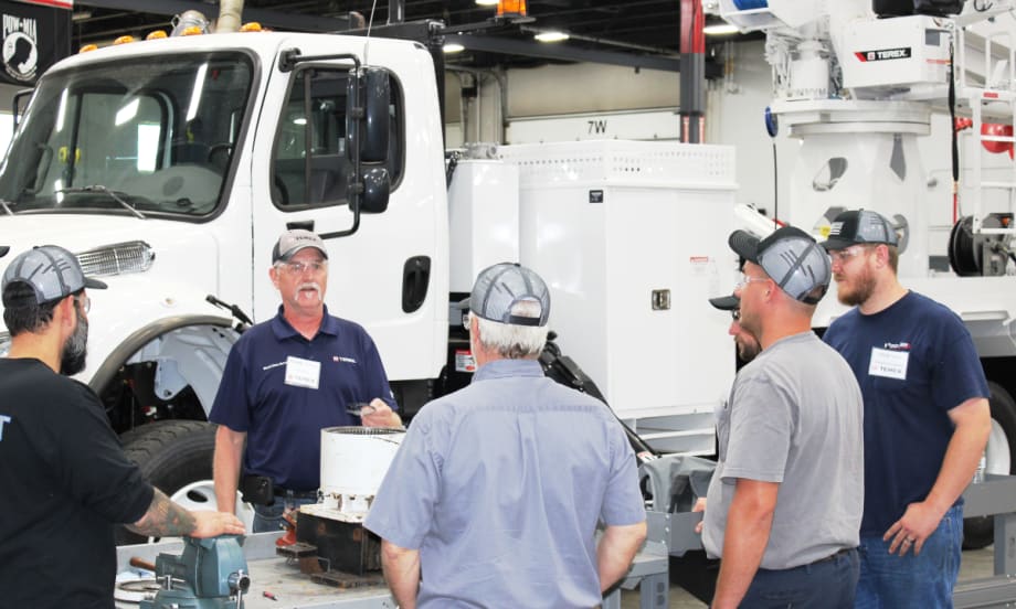 Group of men standing around a bucket truck being trained on maintenance.