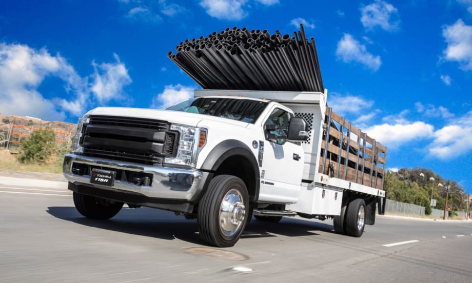 image of a white work truck hauling pipes extending over the cab