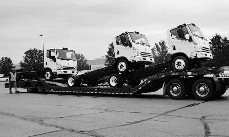 Three chassis cab trucks are shown loaded on a trailer.
