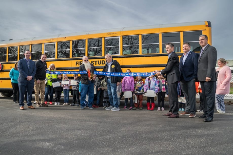 two people in safety vests walk in front of school buses