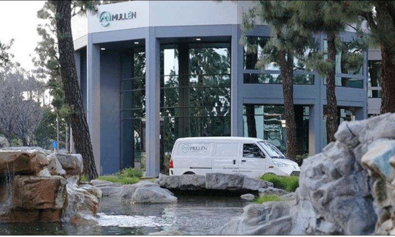 White cargo van parked in front of a landscaped corporate building with Mullen logo.