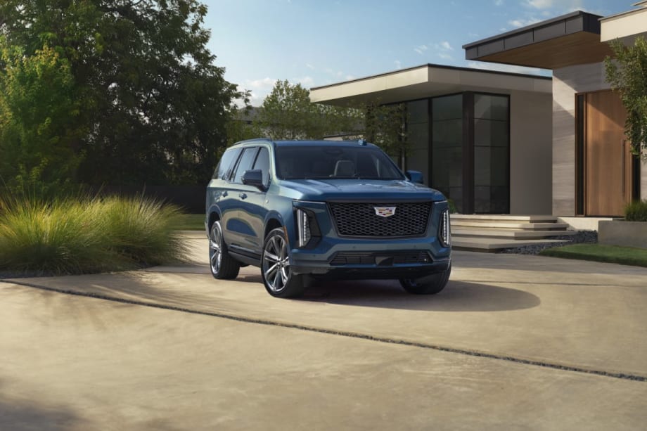 Sunny outdoor shot of a blue 2025 Cadillac Escalade SUV in the drive way of a house.